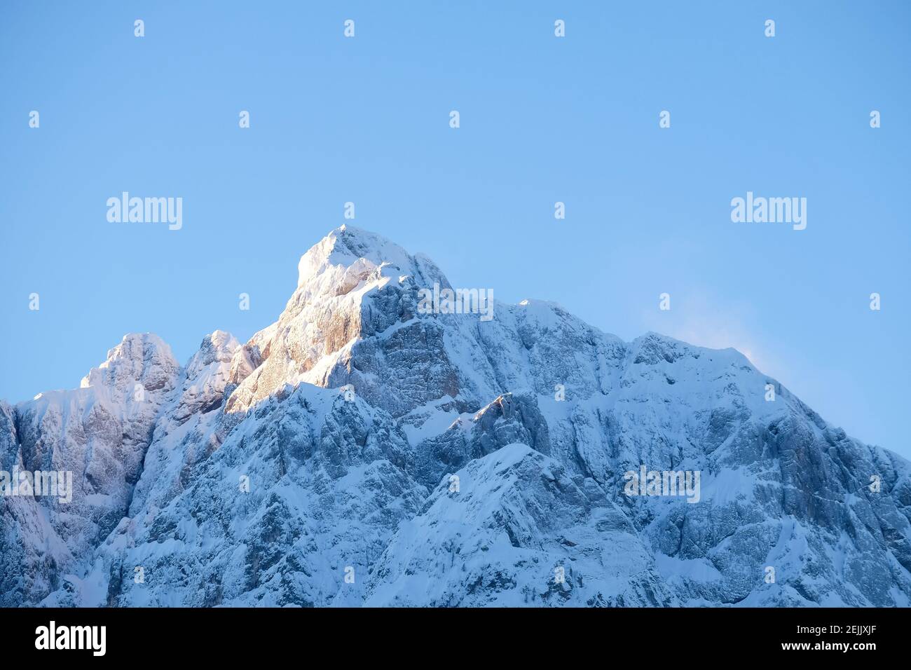 Bellissimo primo piano di un rosa incandescente cime delle Alpi al tramonto, mentre il vento soffia la neve al largo della montagna. Potenza degli elementi naturali Foto Stock