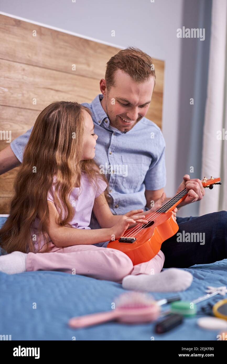 Papà suona la chitarra con la sua figlia piccola. caucasica carino bambino  impara a suonare strumento musicale con il tutor. Duetto musicale di padre  con un bambino ad h Foto stock -