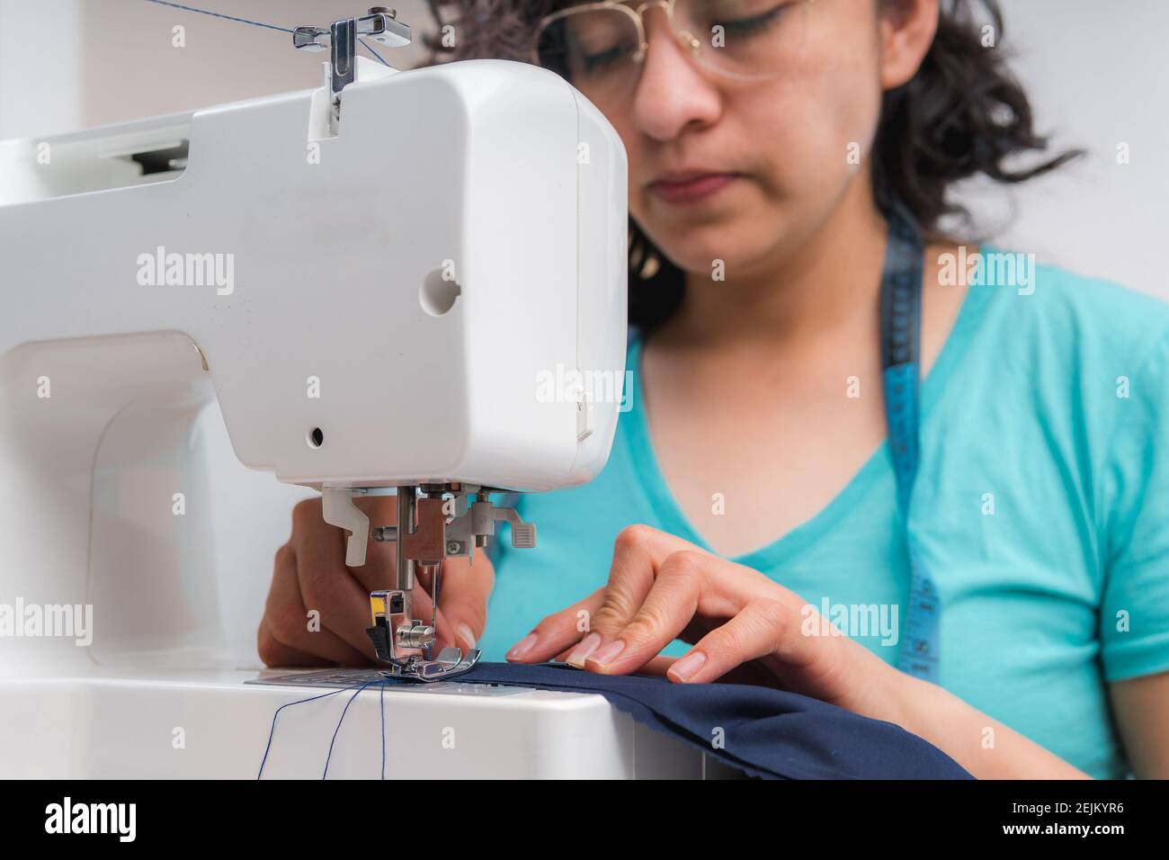 Donna allegra cucire mentre sedeva al suo posto di lavoro dentro laboratorio di moda Foto Stock