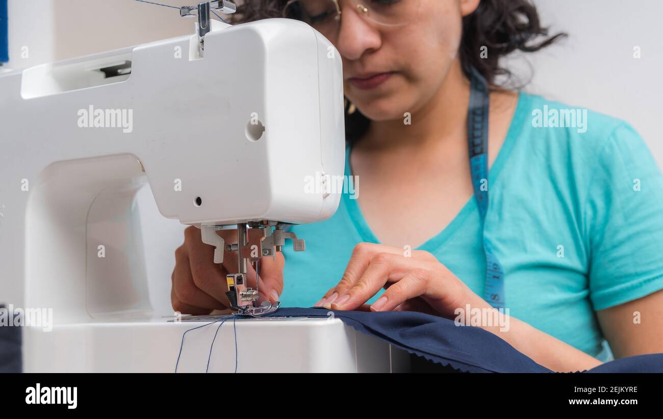 Donna allegra cucire mentre sedeva al suo posto di lavoro dentro laboratorio di moda Foto Stock