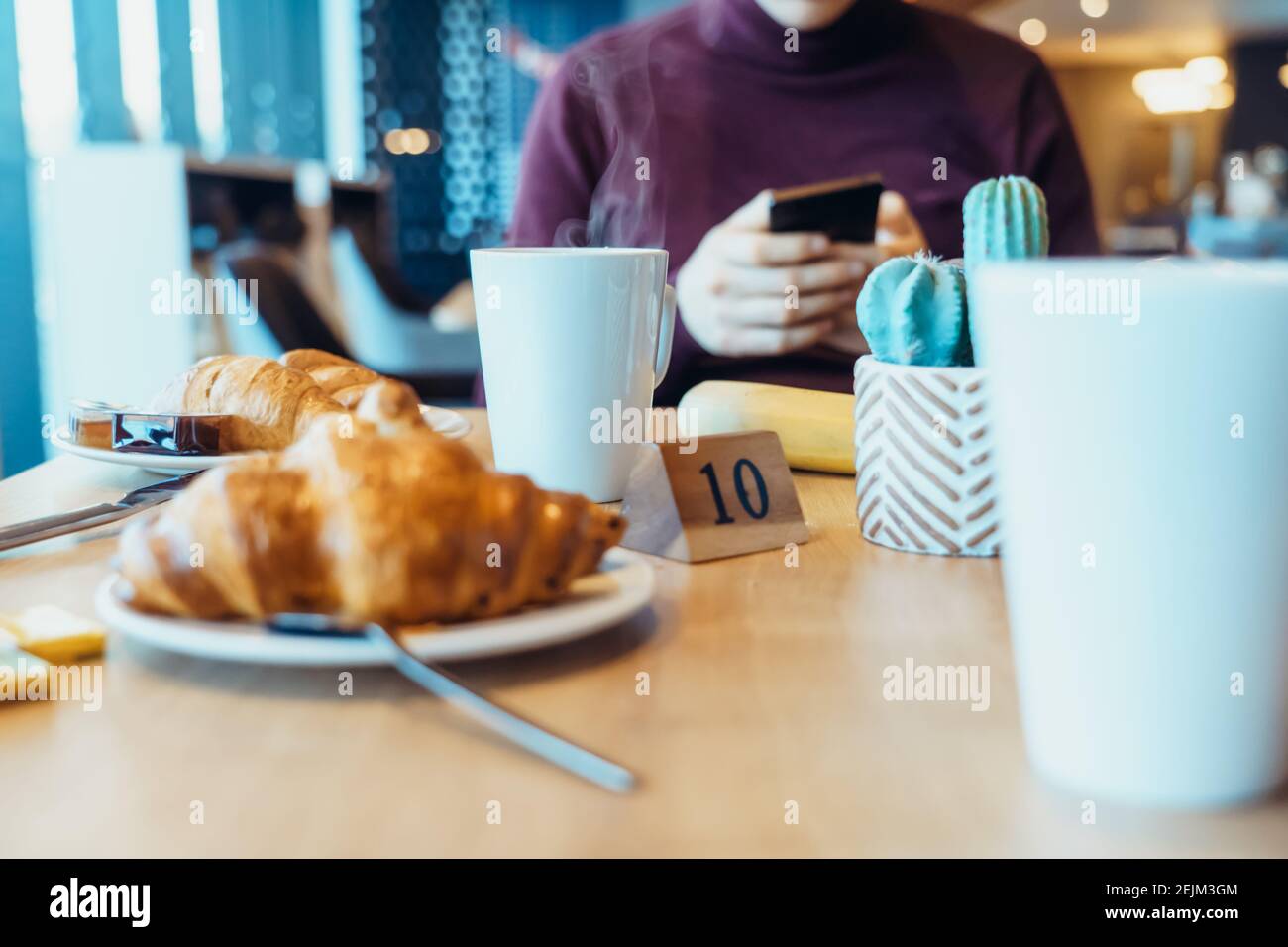 Una tazza di tè caldo e croissant freschi sul tavolo dove il giovane usa il telefono durante la colazione nel ristorante dell'hotel. Messa a fuoco selettiva, Foto Stock