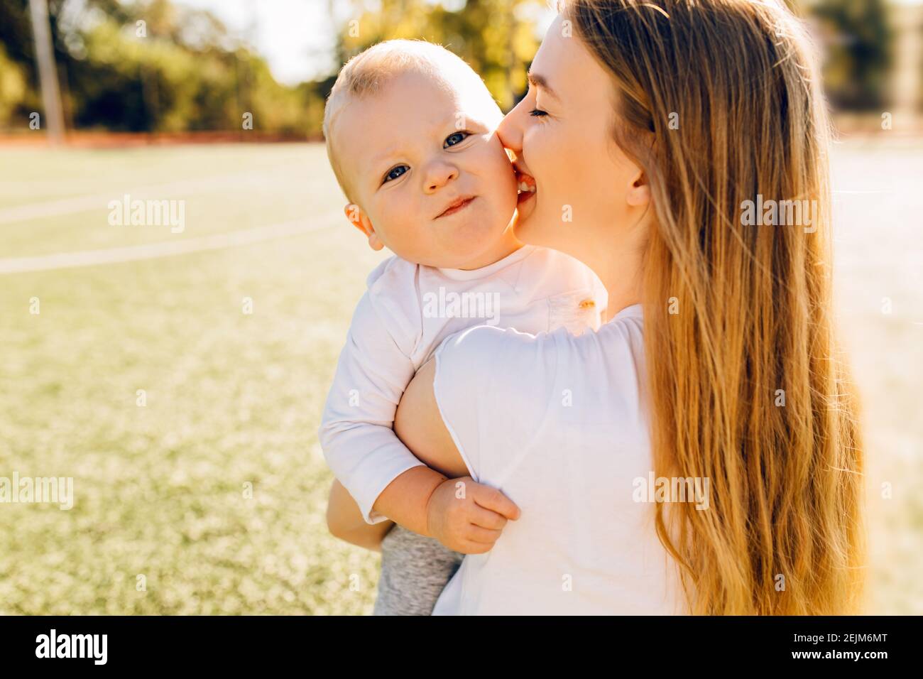 La madre felice bacia e abbracca il suo bambino nel parco in una giornata estiva di sole, giorno della madre Foto Stock