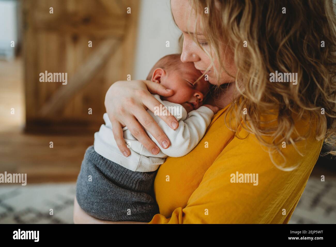 Primo piano di bella mamma bionda che tiene il bambino neonato dentro le braccia Foto Stock