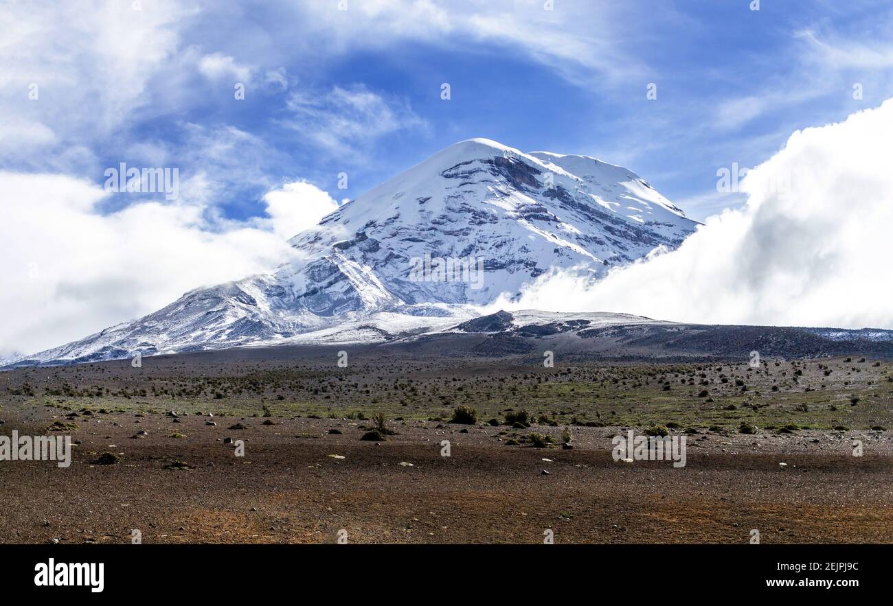 Vulcano Chimborazo innevato nelle Ande dell'Ecuador con un cielo blu circondato da nuvole. Foto Stock