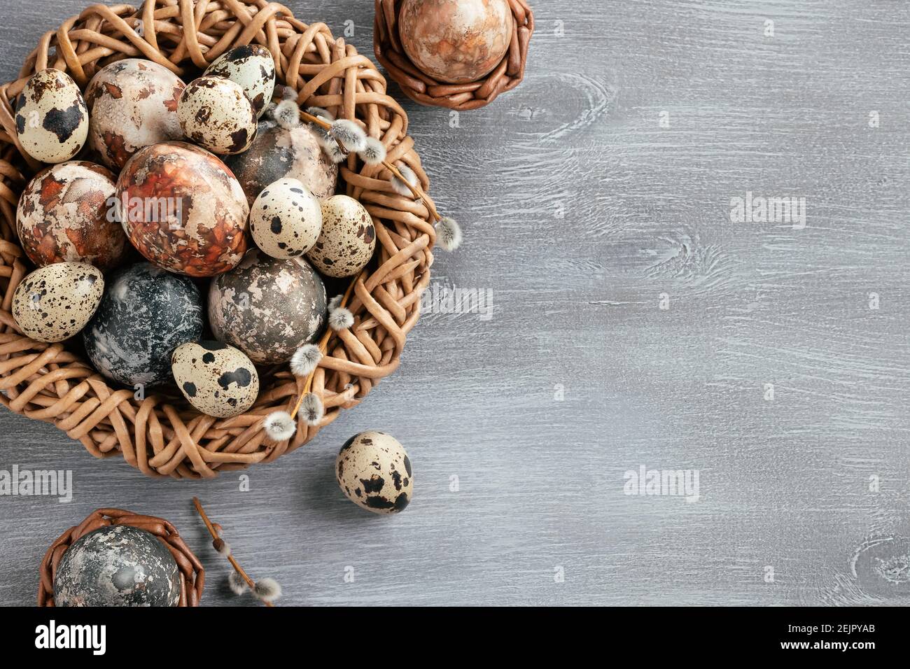 Composizione pasquale - diverse uova di marmo dipinte con coloranti naturali in un nido di vimini e cestini, vista dall'alto. Foto Stock