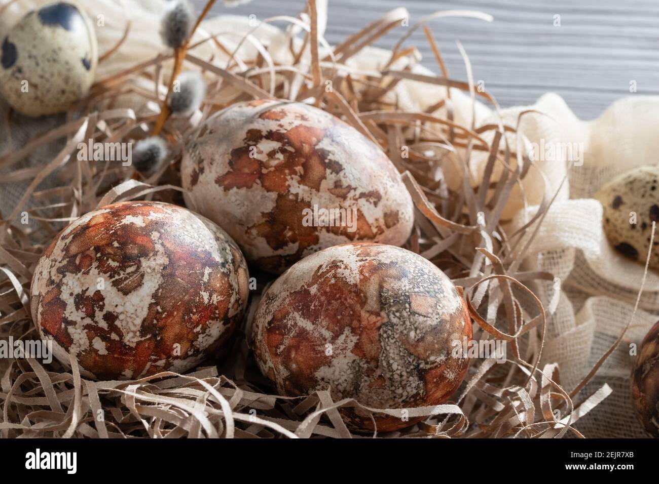 Composizione pasquale - diverse uova di marmo dipinte con coloranti naturali in un nido di carta sul tavolo. Foto Stock