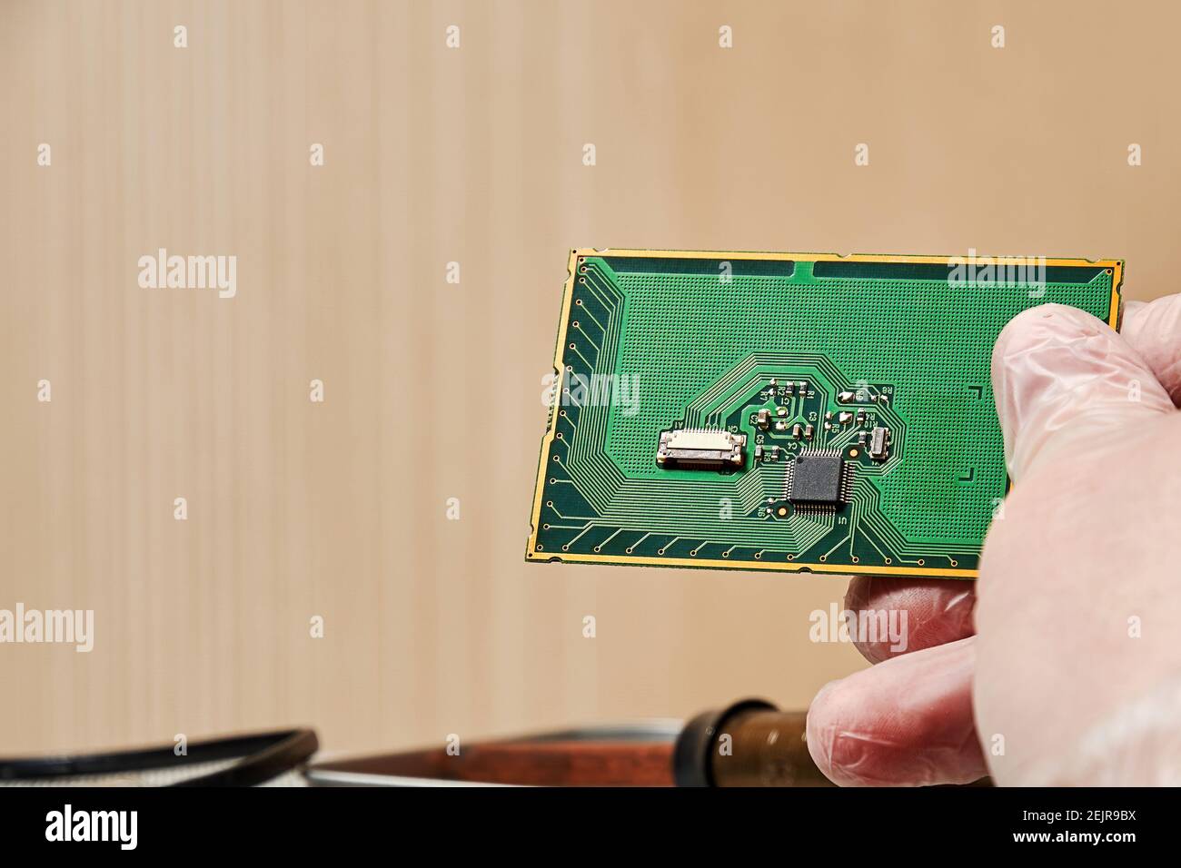 Il lavoratore tiene il circuito stampato con un chip nella mano sopra il tavolo del laboratorio. Concetto e simboli di fabbricazione e nanotecnologia Foto Stock