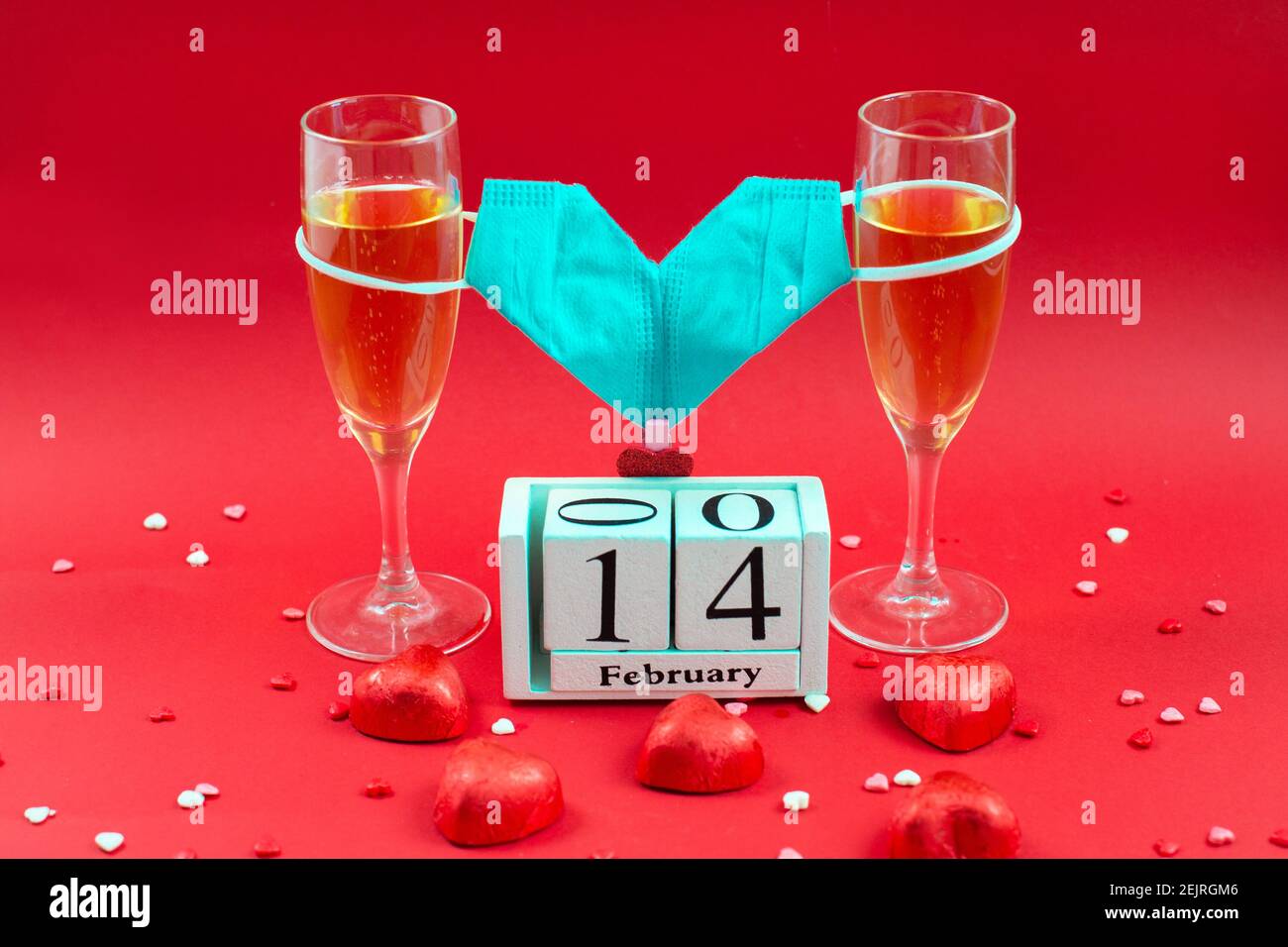 Due glasi champagne, calendario in legno, caramella e maschera medica valentina su sfondo rosso. 14 febbraio 2021. Data romantica. Concept San Valentino. Foto Stock