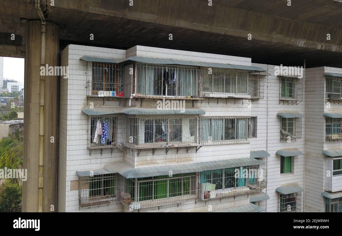 Una vista aerea di una fila di edifici di appartamenti che si erigono sotto un viadotto come moli, la città di Guiyang, provincia di Guizhou della Cina orientale, 11 marzo 2020. La scena unica è dovuta al trucco dello sviluppatore del bene immobile. Lo sviluppatore ha vinto l'offerta di costruire la strada per l'aeroporto, e ha promesso ai residenti che avevano vissuto sulla strada che il risarcimento sarebbe stato pagato dopo la costruzione. Tuttavia, la compensazione si è rivolta agli edifici di appartamenti che si trovarono sotto un viadotto sulla strada per l'aeroporto. I residenti devono prendere il risultato, ma disperatamente per muoversi fuori dal traffico sul viadotto influenzano la loro vita quotidiana Foto Stock