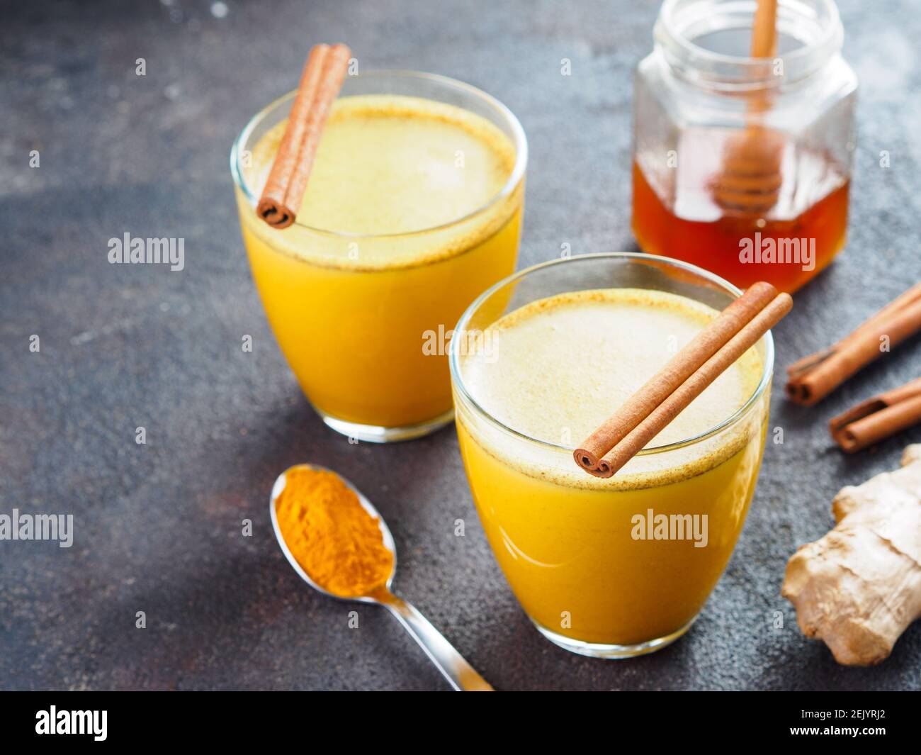 Bevanda sana latte curcero dorato in vetro.latte d'oro con curcuma,zenzero Radice, bastoncini di cannella, polvere curcuma e miele su cemento nero background.detox curcuma tè e Ingredients.CopySpace Foto Stock
