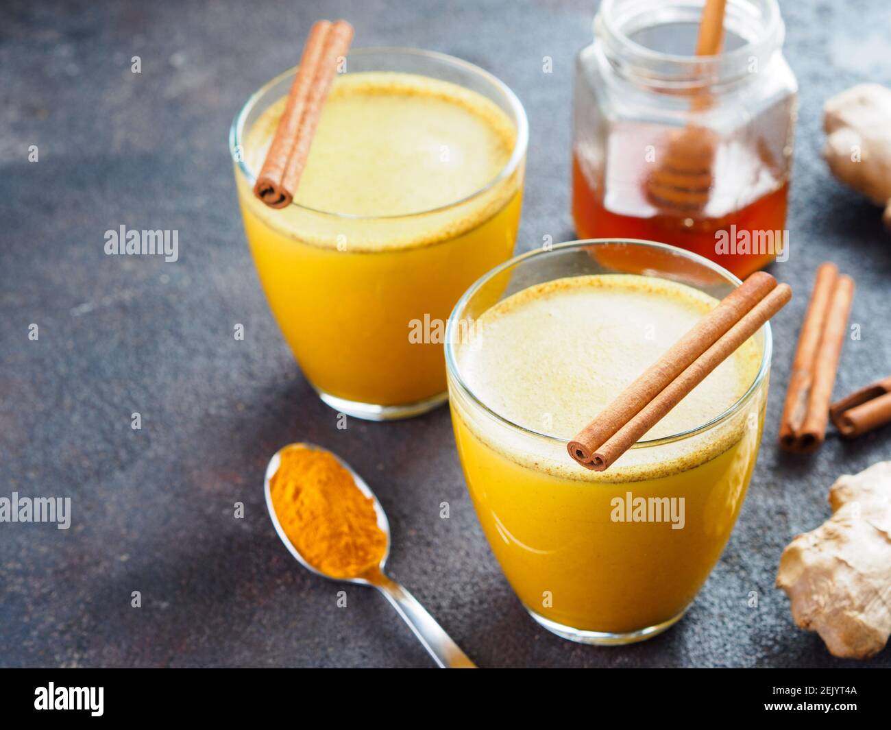 Bevanda sana latte curcero dorato in vetro.latte d'oro con curcuma,zenzero Radice, bastoncini di cannella, polvere curcuma e miele su cemento nero background.detox curcuma tè e Ingredients.CopySpace Foto Stock