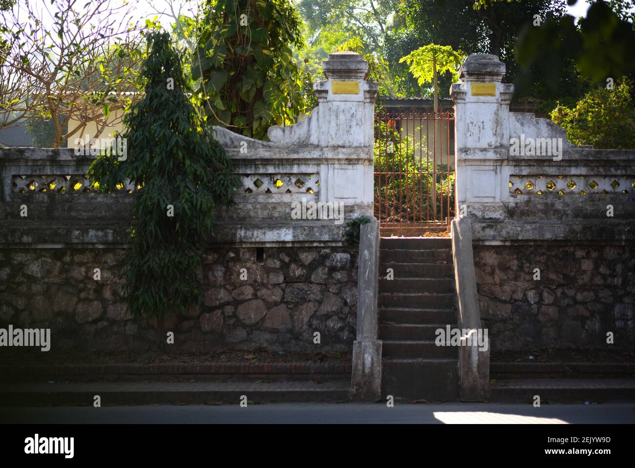Parco soleggiato che appare dietro un muro con cancello chiuso, pochi gradini che conducono al cancello. Dietro il Museo Nazionale di Luang Prabang, Laos Foto Stock