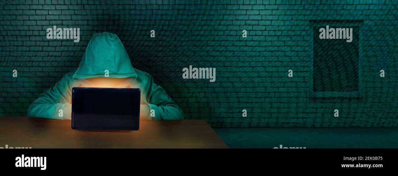 L'hacker lavora dietro uno schermo del laptop in una stanza con una parete di mattoni. Criminalità su Internet. Il concetto di hacking e malware, sicurezza informatica. Crimini digitali Foto Stock