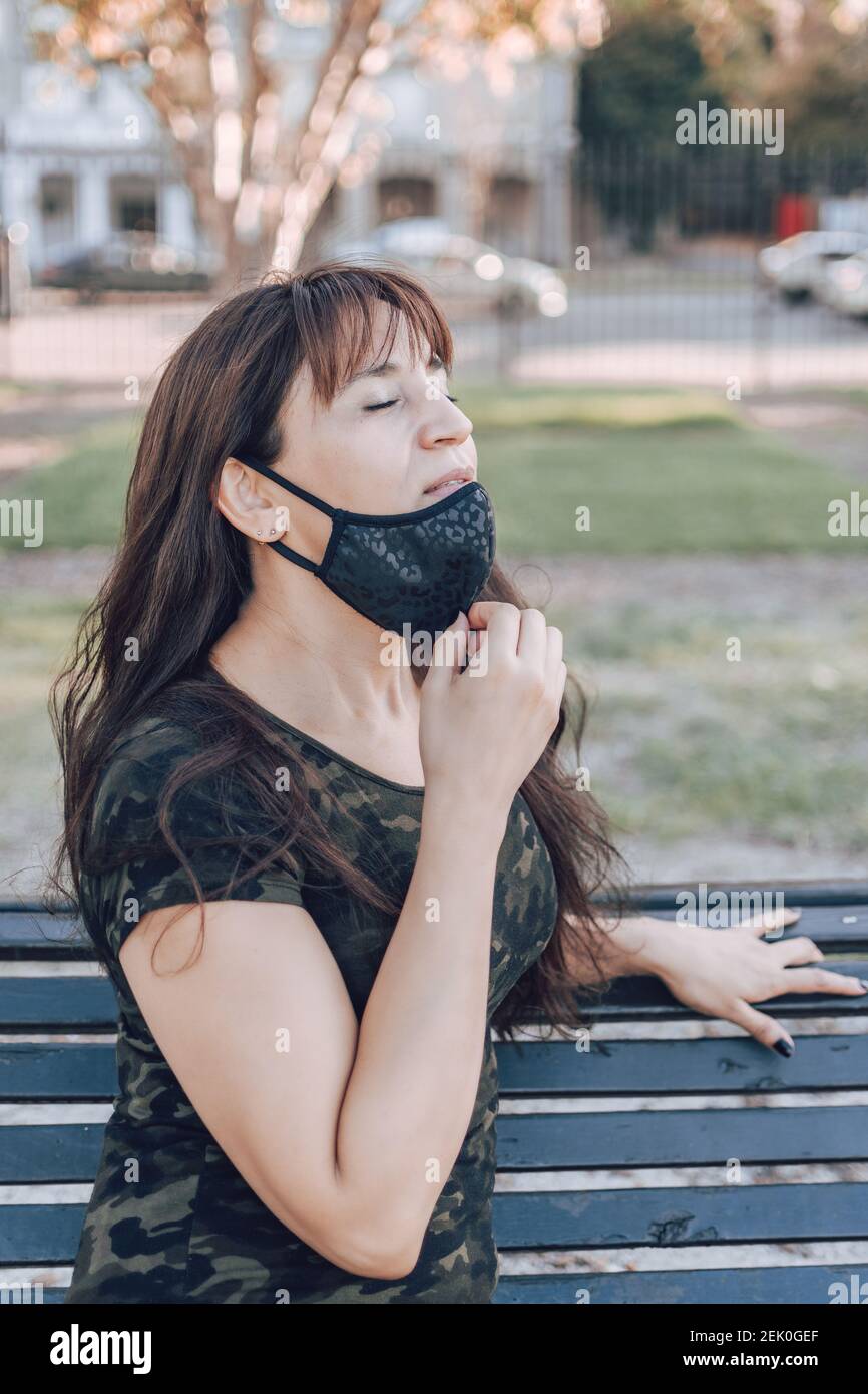 Una donna latina rimuove la maschera protettiva dal viso per respirare aria pulita e fresca. Foto Stock