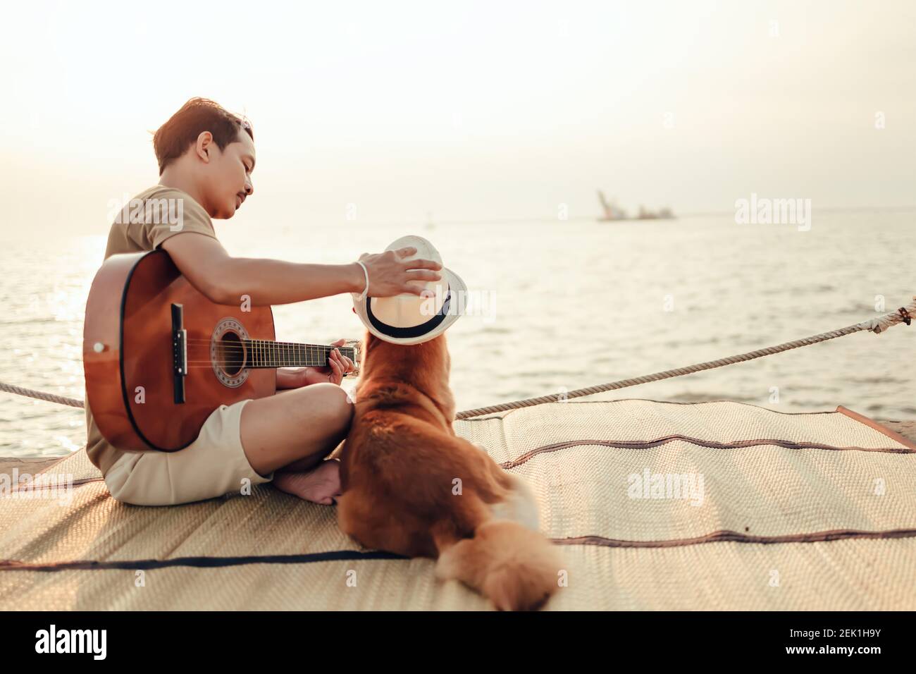 Un uomo suona la canzone della chitarra vicino al tramonto sul mare e prova  a indossare il cappello nella testa del cane. Viaggio, vocazione, concetto  di vacanza Foto stock - Alamy