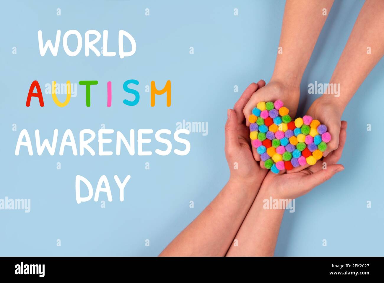 Concetto del giorno di consapevolezza dell'autismo del mondo - mani del bambino autistico sostenute dalla madre che tiene il cuore multicolore su sfondo blu. Spettro autismo Foto Stock