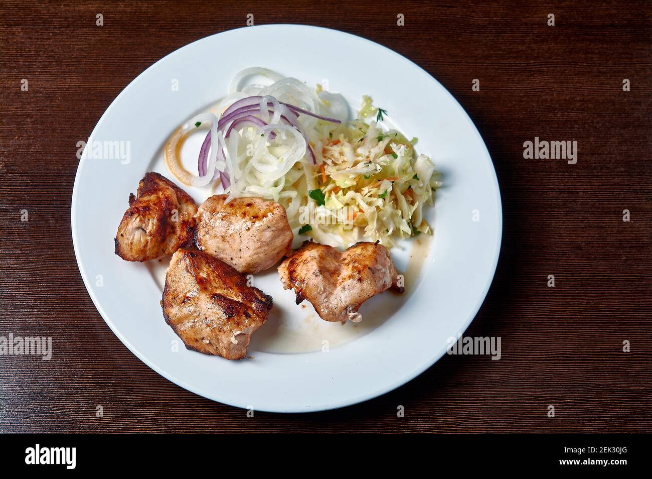 sgranate il kebab con insalata e cipolle su un piatto bianco su sfondo scuro Foto Stock