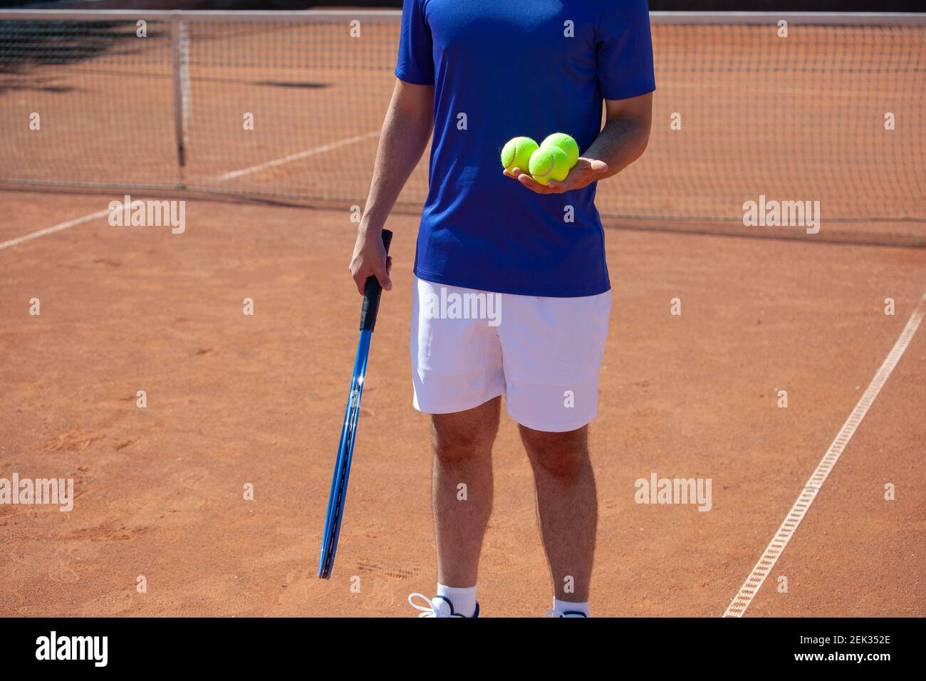 Giocatore di tennis che tiene una racchetta da tennis e tre palle sopra un campo da tennis in terra battuta Foto Stock