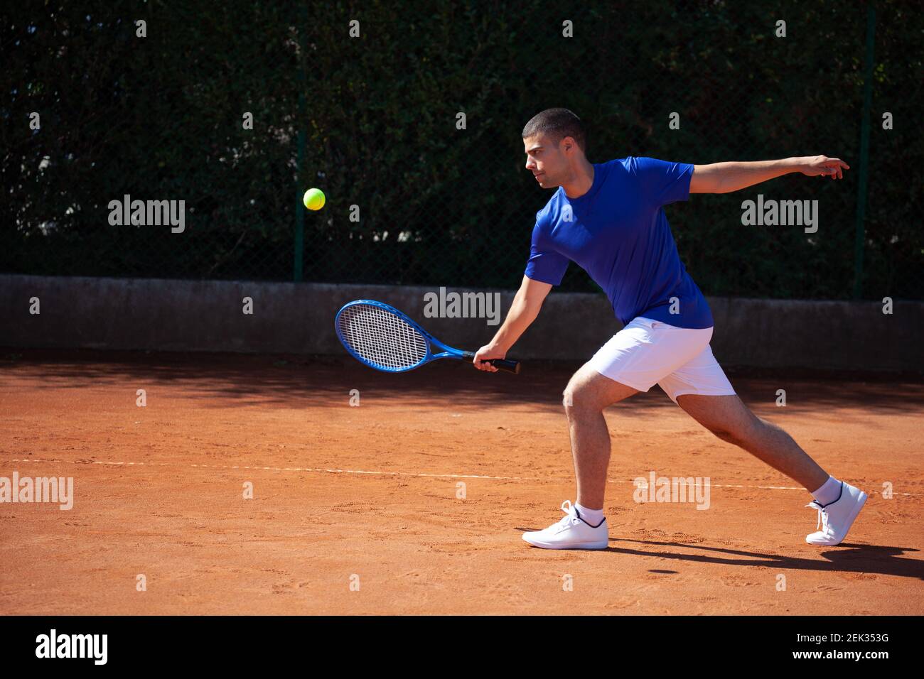 Il giovane giocatore di tennis sportivo incontra un tiro dell'avversario su un campo di gioco di argilla Foto Stock
