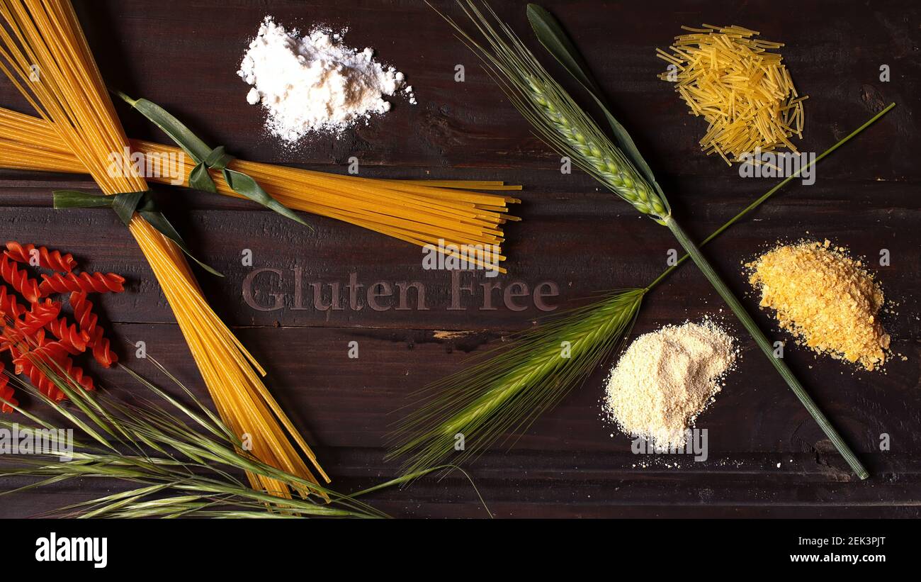 Concetto di cibo sano, vari tipi di farine raffinate e pasta senza glutine su sfondo di legno scuro con diverse orecchie di grano e orzo verde Foto Stock