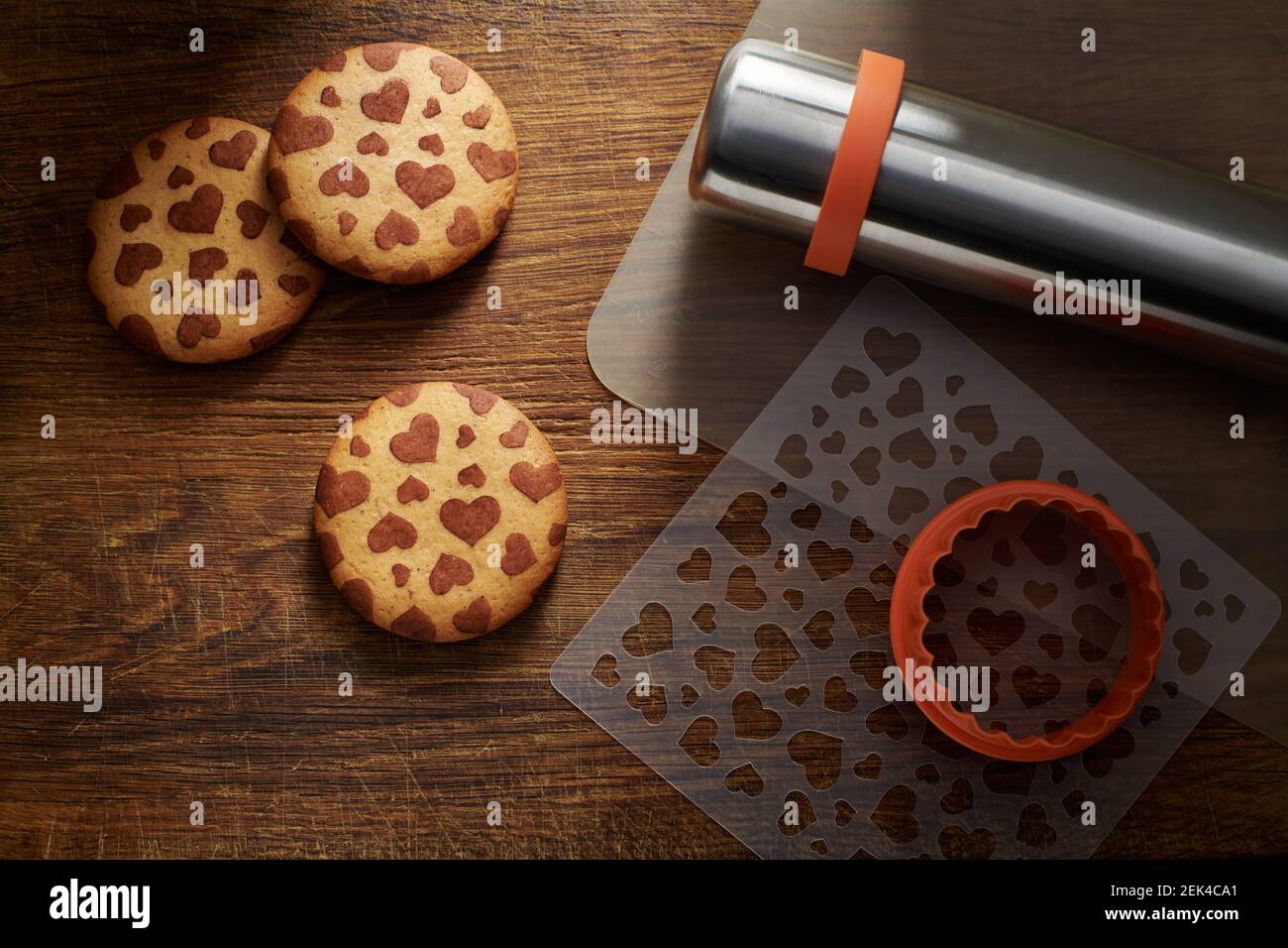 Biscotti con motivo a forma di cuore, taglierina per biscotti, stampino, stuoia da forno, spilla su una superficie di legno marrone Foto Stock