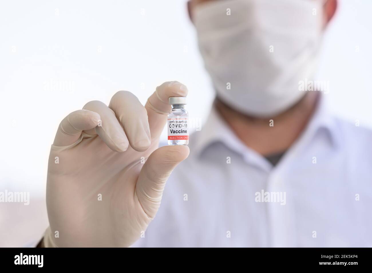 Il medico con guanti bianchi contiene un flacone con vaccino COVID-19. Concetto di medicina, sperimentazione clinica e trattamento dovuto al coronavirus SARS-COV-2. Sfocatura Foto Stock