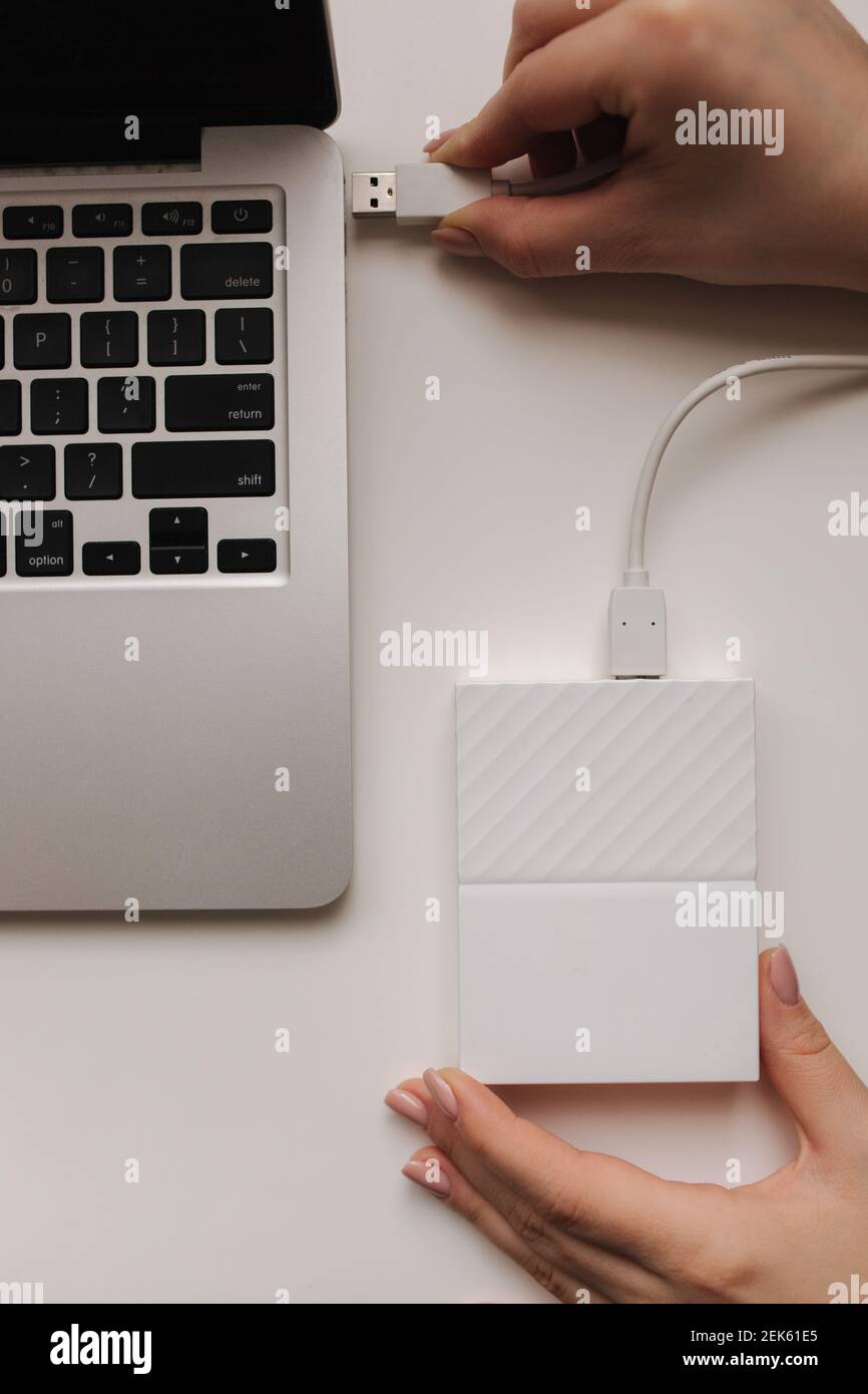 Disco rigido portatile femmina collegato a mano al computer portatile per il trasferimento dei dati. File di backup. Copia file. Vista dall'alto Foto Stock