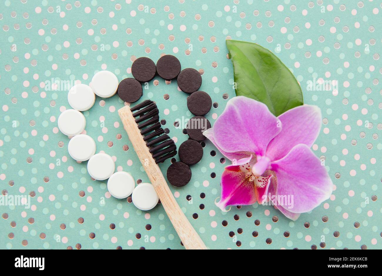 Vista dall'alto delle compresse di dentifricio al carbone attivo nero e al fluoruro bianco. Concetto di cura dentale. Sfondo minato verde menta con orchidea rosa Foto Stock