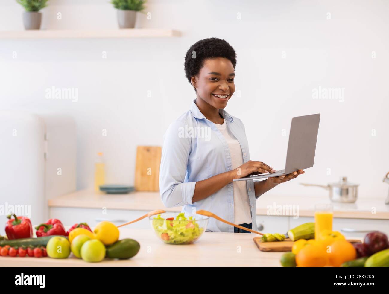 African Lady Holding laptop Browsing Ricette cena di cucina Foto Stock