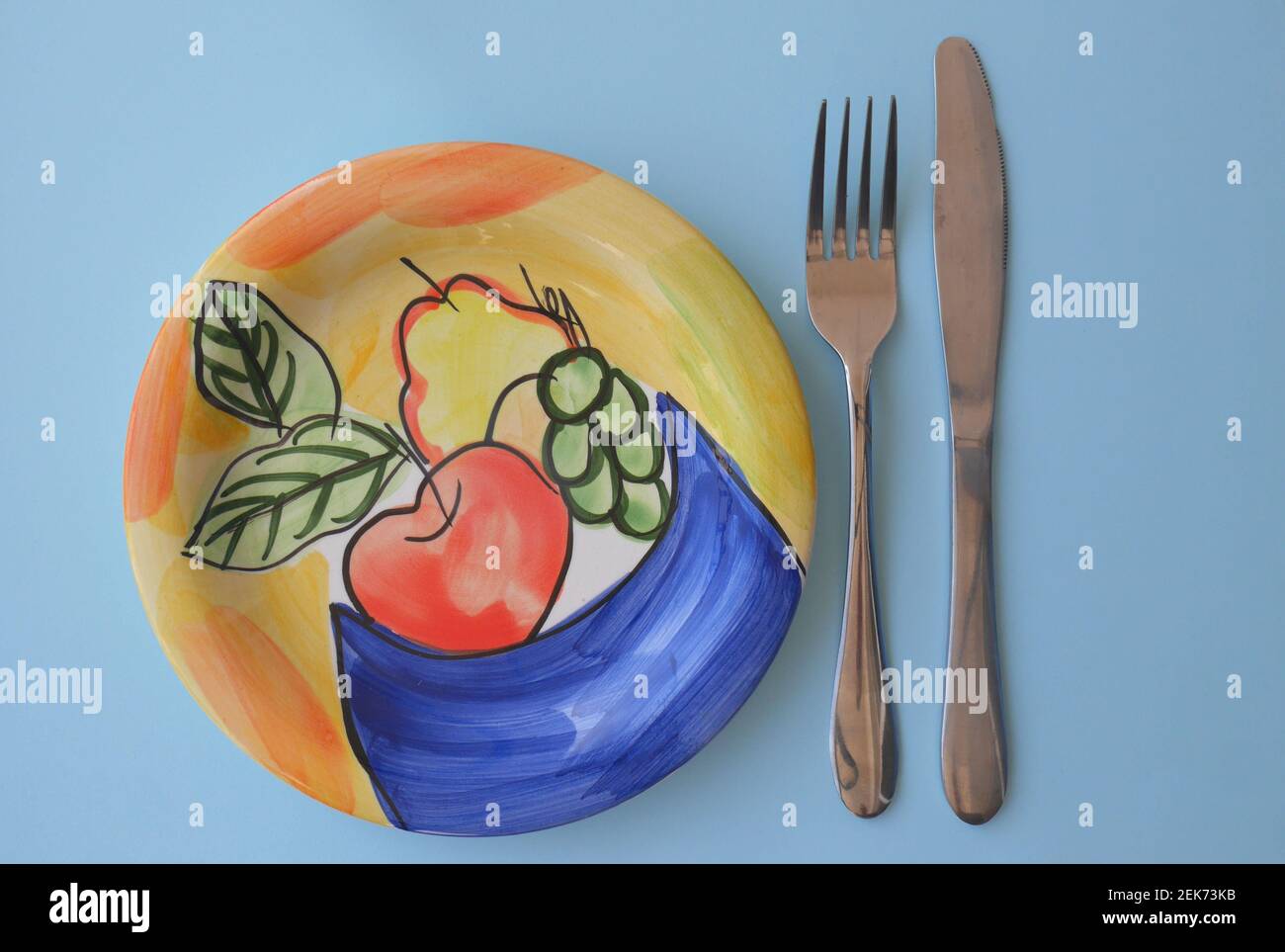 Piastra laterale vuota in ceramica con disegno fruttato, coltello e forchetta Foto Stock