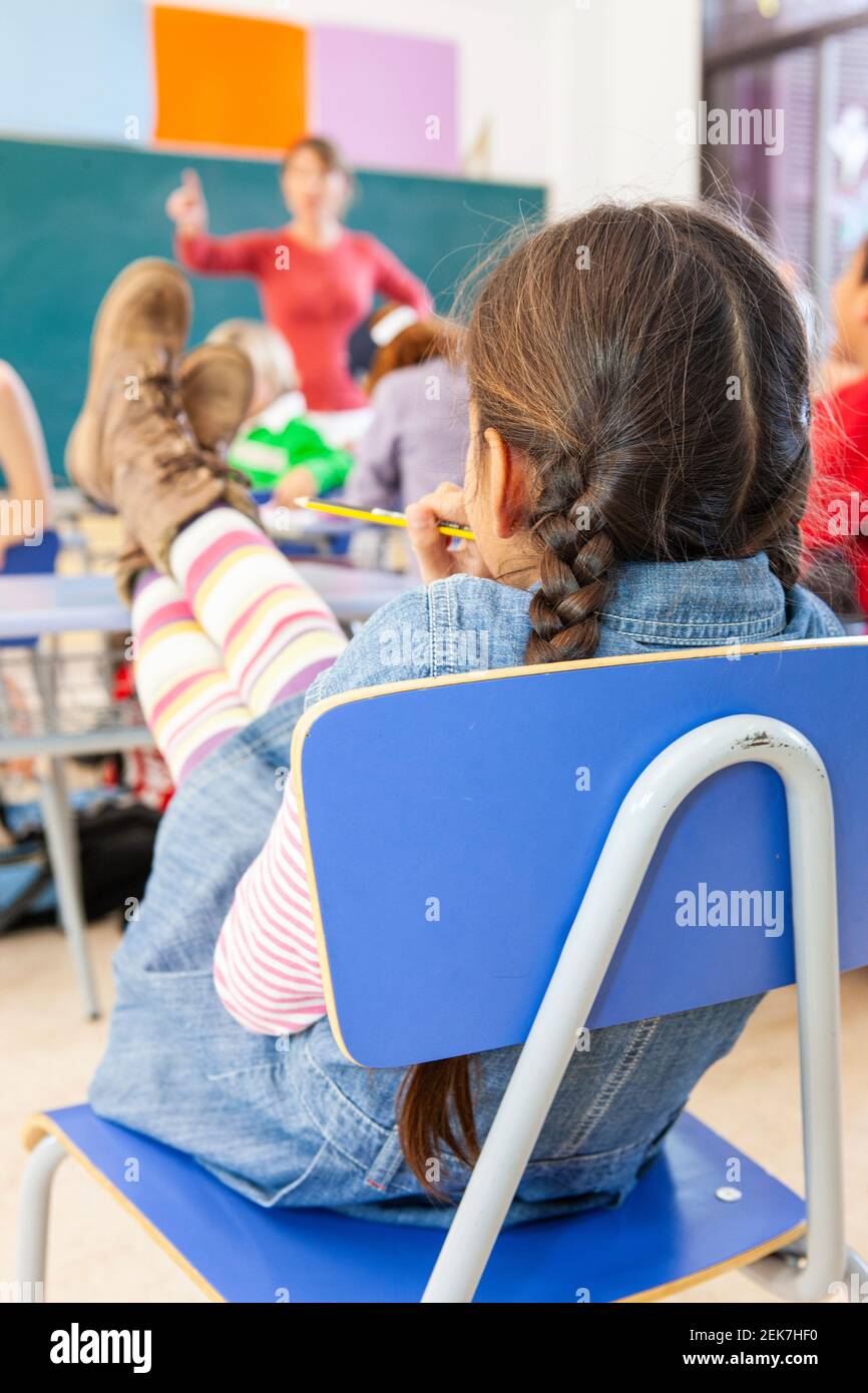 Ragazza giovane con i piedi su una scrivania dentro un'aula scolastica Foto Stock
