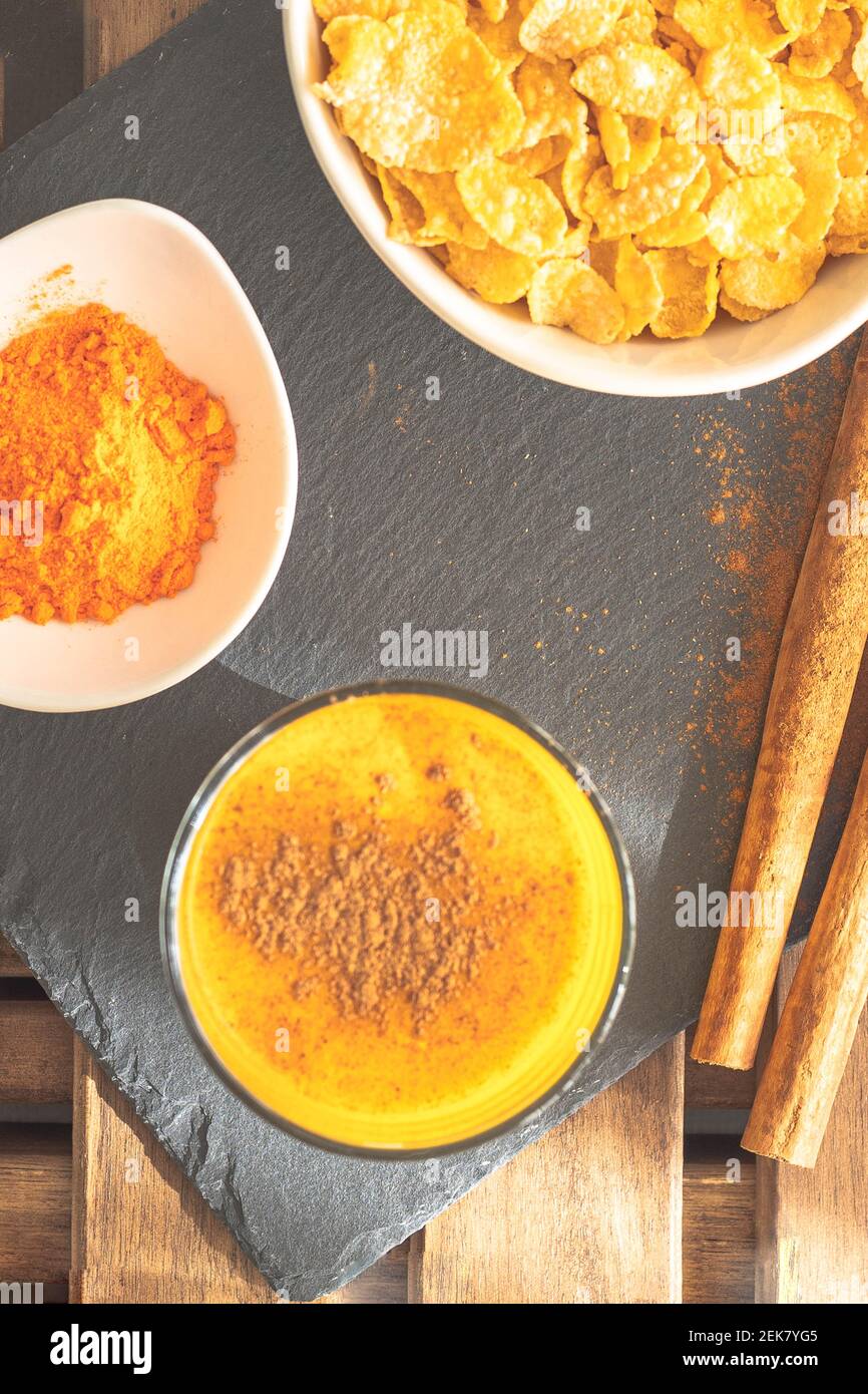 zenith shot di una colazione con curcuma dorato e cannella Latte di origine indiana con una ciotola di fiocchi di mais su un tavolo di legno Foto Stock