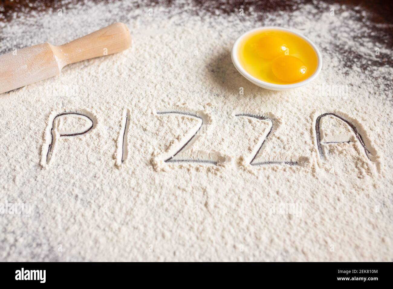 L'iscrizione Pizza su farina spruzzata, disegnata su fondo di legno, spilla e uova. Ricette di cottura. . Foto di alta qualità Foto Stock