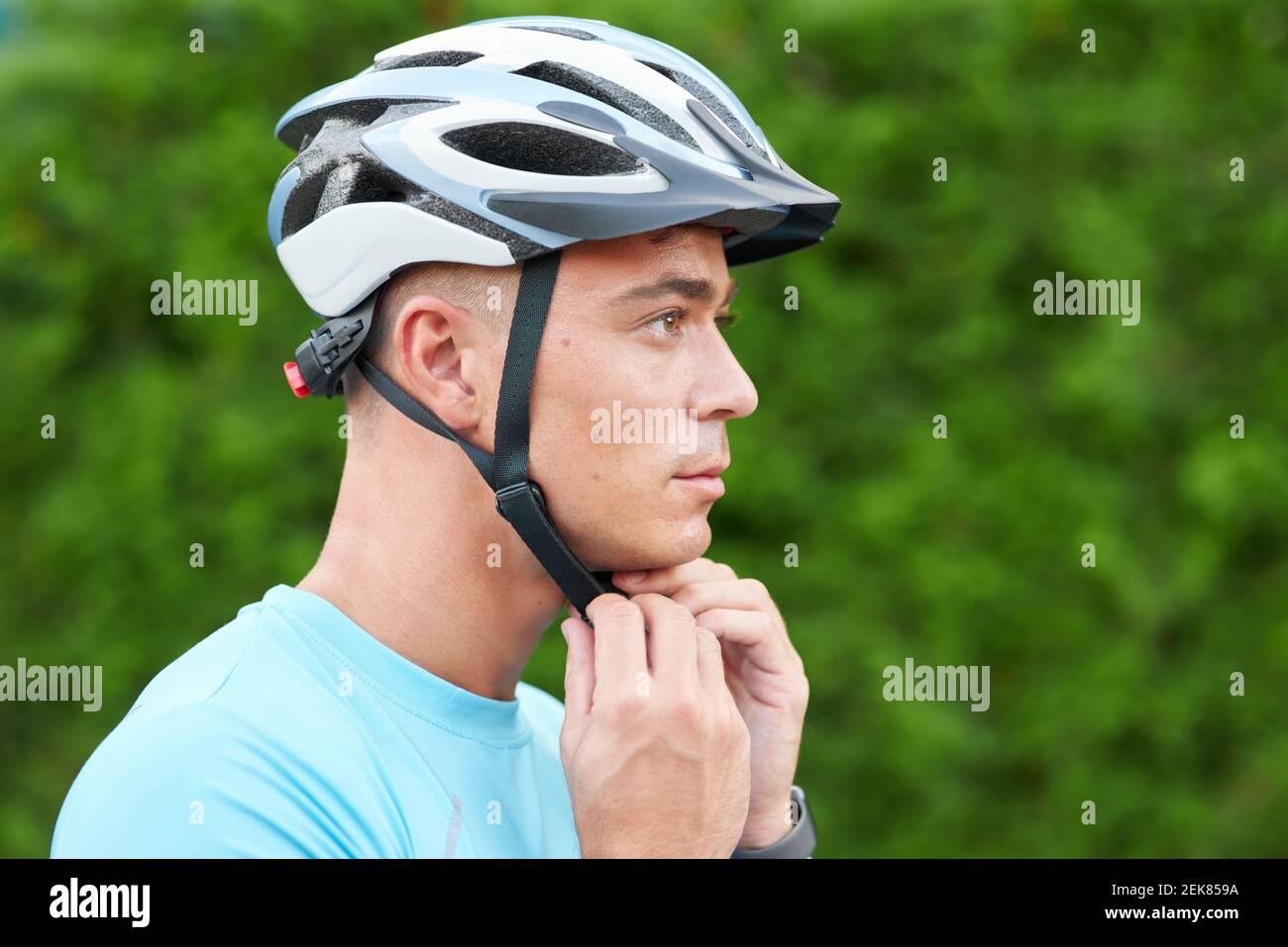 Preparati. Ritratto di bel ciclista maschile che mette il casco sulla testa, preparandosi, in piedi all'aperto in natura. Sport, ciclismo, concetto di persone. Vista laterale Foto Stock