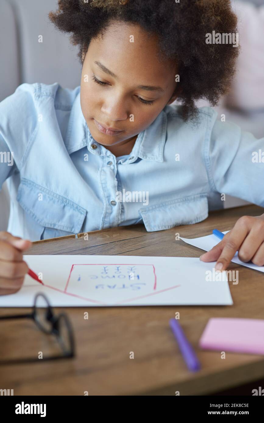 Razza mista teen scolargirl disegno su carta con marcatori colorati mentre si passa il tempo a casa durante la quarantena Foto Stock