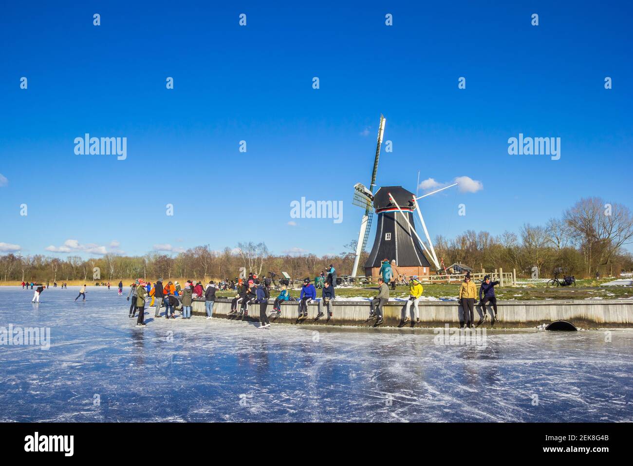 Mulino a vento e persone che si preparano a pattinare al lago Paterswoldse Meer a Groningen, Paesi Bassi Foto Stock