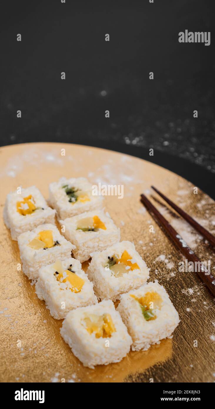 Consegna sushi. Panini dolci a base di riso, ananas, kiwi e mango. Rotola su sfondo oro e nero. Bastoncini di legno per sushi. Foto Stock