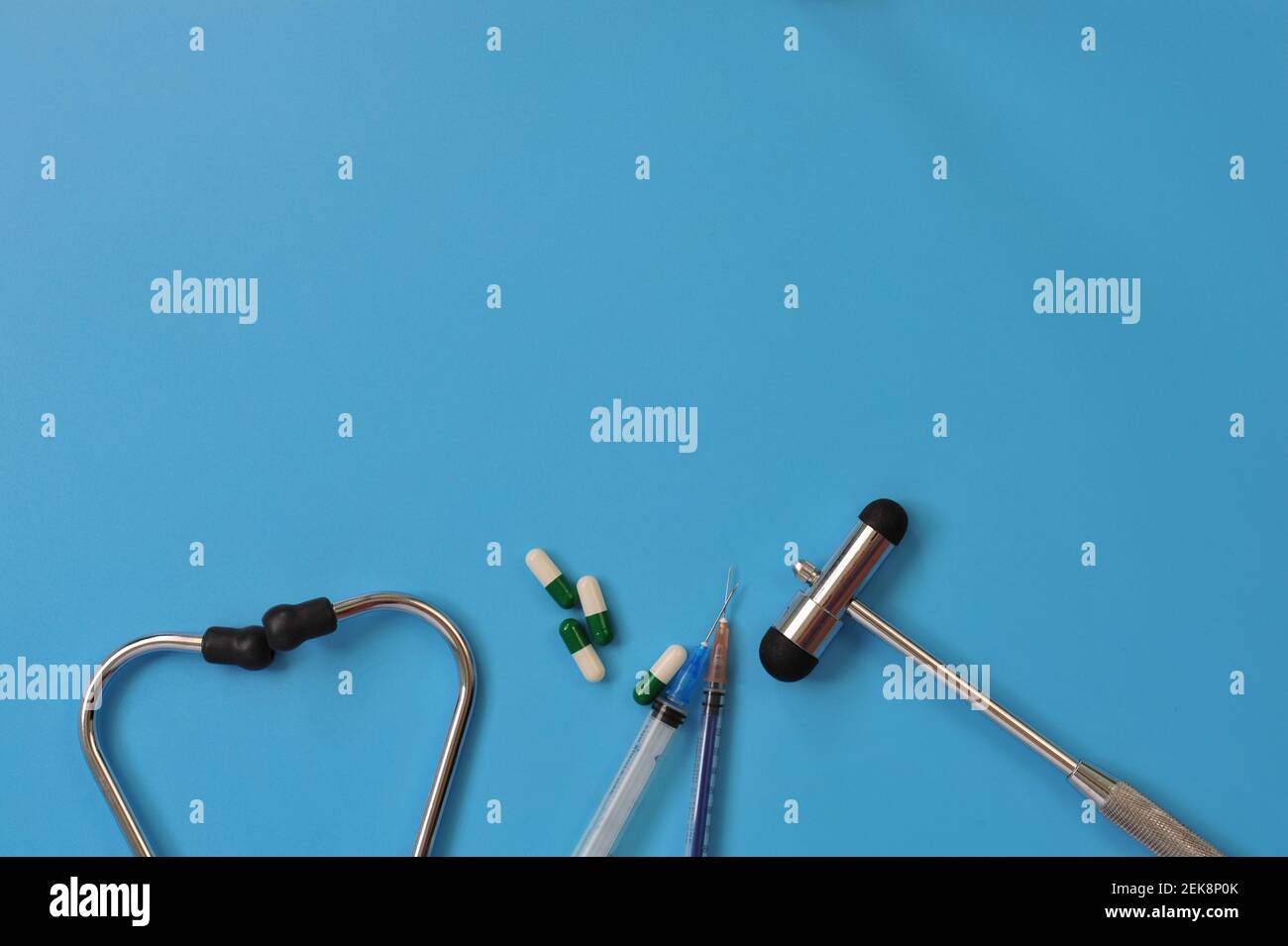 Layout di stetoscopio, martello reflex, siringhe e pillole con spazio vuoto per il testo su sfondo blu Foto Stock