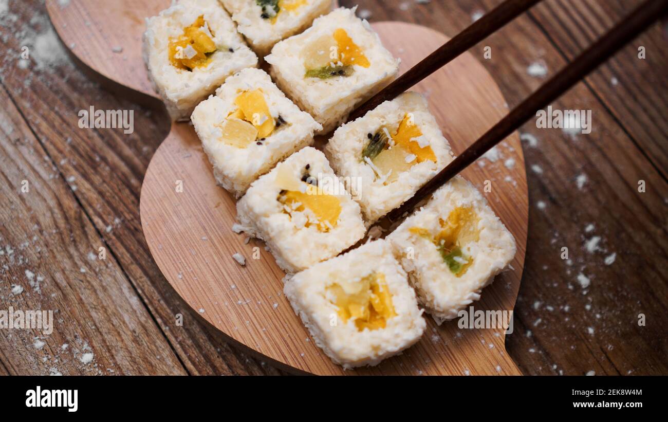 Consegna sushi. Panini dolci a base di riso, ananas, kiwi e mango. Rotola su uno sfondo di legno. Bastoncini di legno per sushi. Foto Stock