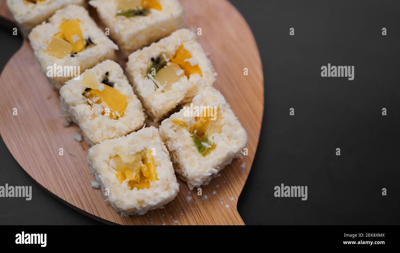 Consegna sushi. Panini dolci a base di riso, ananas, kiwi e mango. Rotola su uno sfondo nero Foto Stock