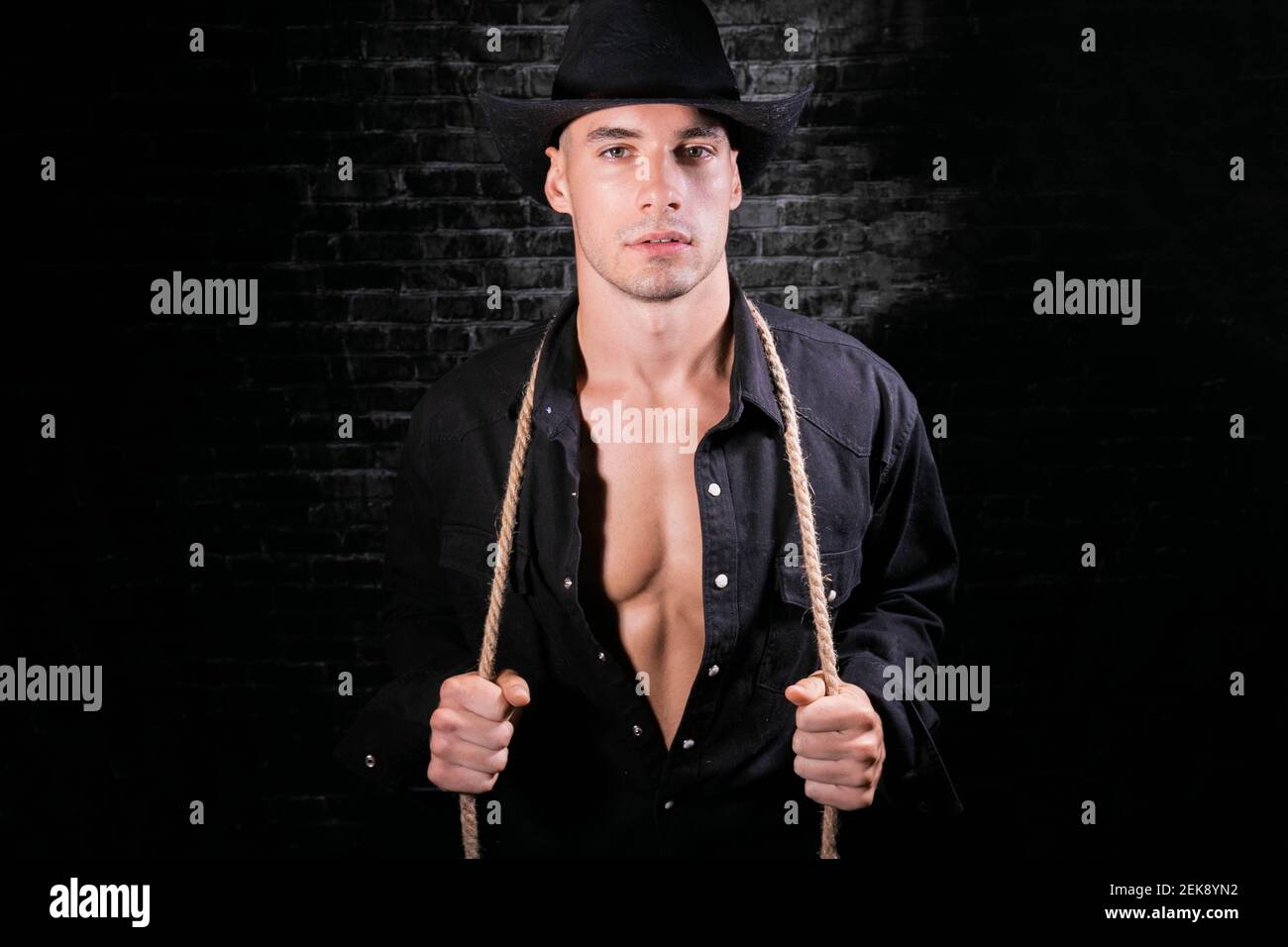 Ritratto di cowboy attraente guardando la fotocamera con camicia aperta nera che rivela pettorina definita e ssixpack abs Foto Stock