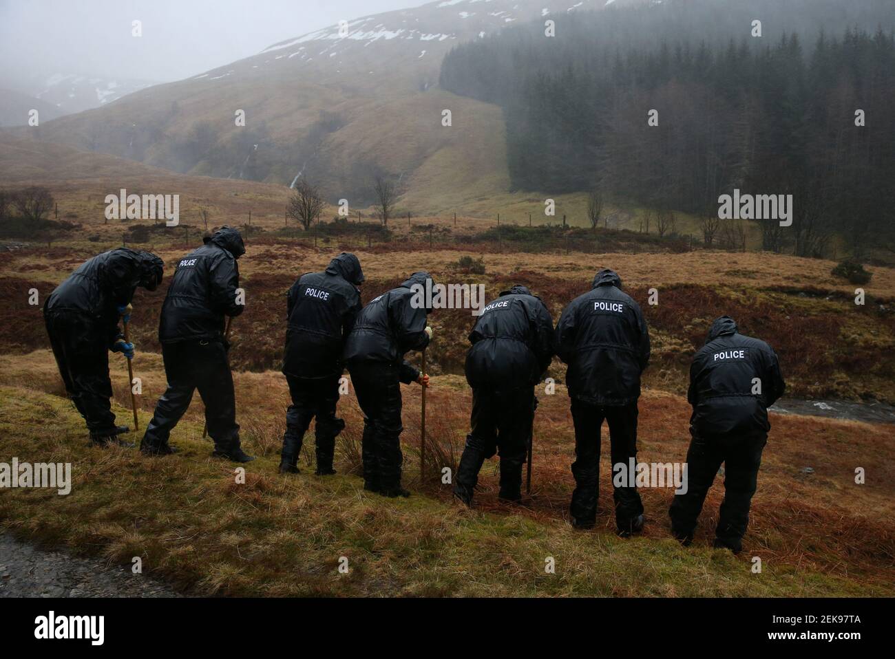 Gli ufficiali di polizia cercano la sottobosco in una valle alla periferia di Tyndrum, mentre altri ufficiali distribuiscono poster e volantini a Tyndrum, Stirlingshire, facendo appello per informazioni su Tony Parsons scomparso mentre si pedalava dalla sua casa a Tillicoultry, Stirlingshire, a Fort William nel settembre 2017. I resti del signor Parsons sono stati scoperti in un'area remota di terreno vicino ad una fattoria vicino alla A82 al Ponte di Orchy il 12 gennaio. Data immagine: Martedì 23 febbraio 2021. Foto Stock