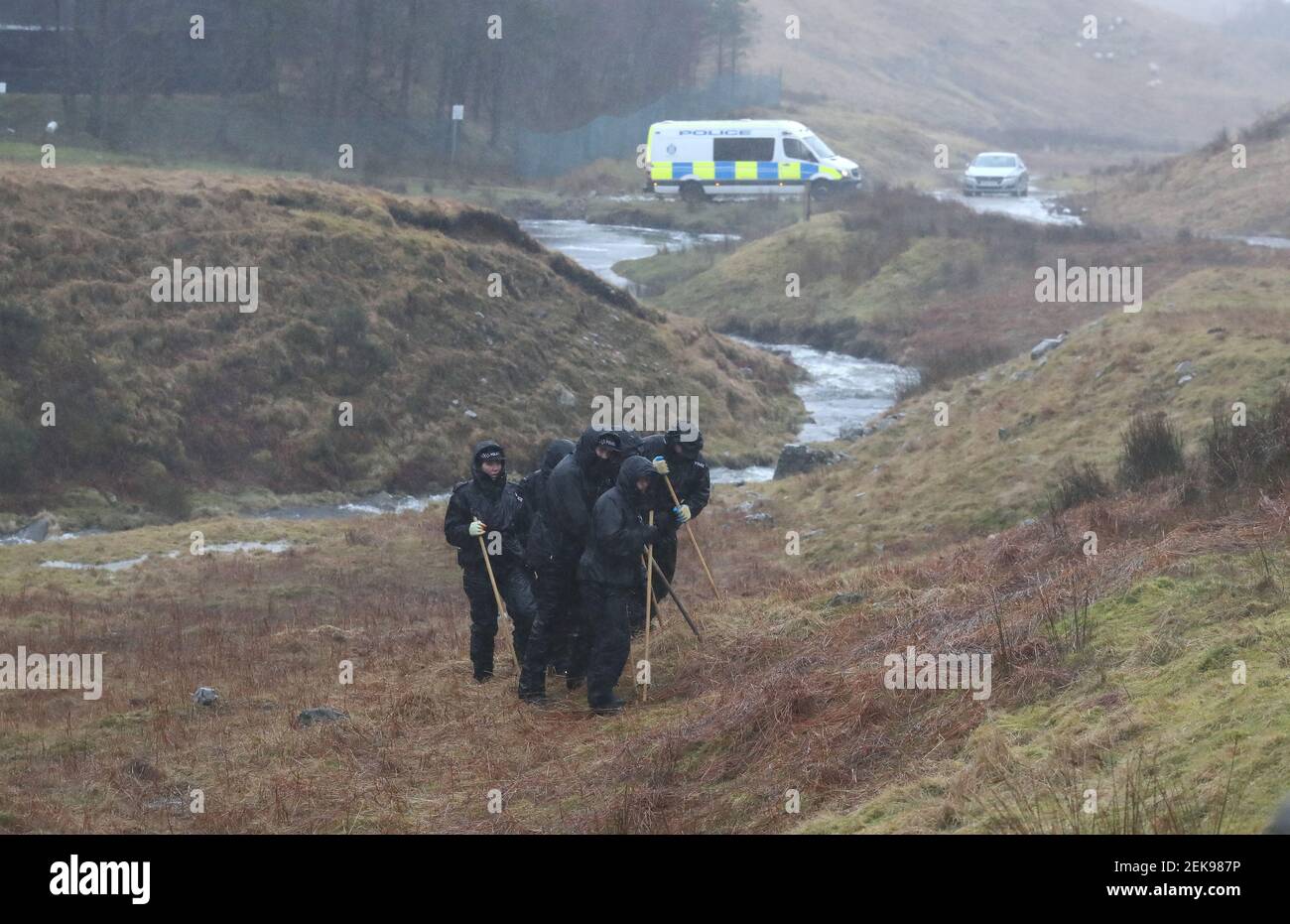 Gli ufficiali di polizia cercano la sottobosco in una valle alla periferia di Tyndrum, mentre altri ufficiali distribuiscono poster e volantini a Tyndrum, Stirlingshire, facendo appello per informazioni su Tony Parsons scomparso mentre si pedalava dalla sua casa a Tillicoultry, Stirlingshire, a Fort William nel settembre 2017. I resti del signor Parsons sono stati scoperti in un'area remota di terreno vicino ad una fattoria vicino alla A82 al Ponte di Orchy il 12 gennaio. Data immagine: Martedì 23 febbraio 2021. Foto Stock