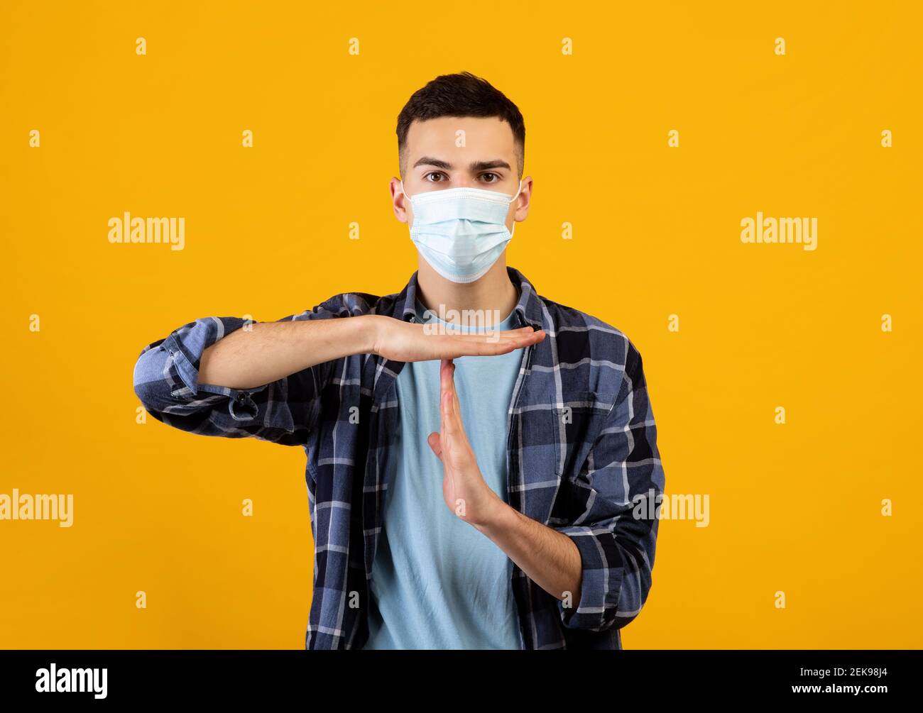 Arresto covid-19. Un ragazzo caucasico che indossa una maschera protettiva per il viso, UN ARRESTO gesturante o UN TIMEOUT per la fotocamera su sfondo arancione Foto Stock