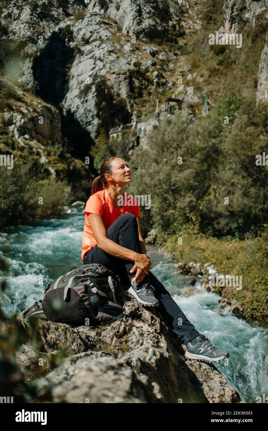 Donna mid adult che guarda via mentre si siede sul fiume a Cares Trail nel Parco Nazionale di Picos De Europe, Asturias, Spagna Foto Stock