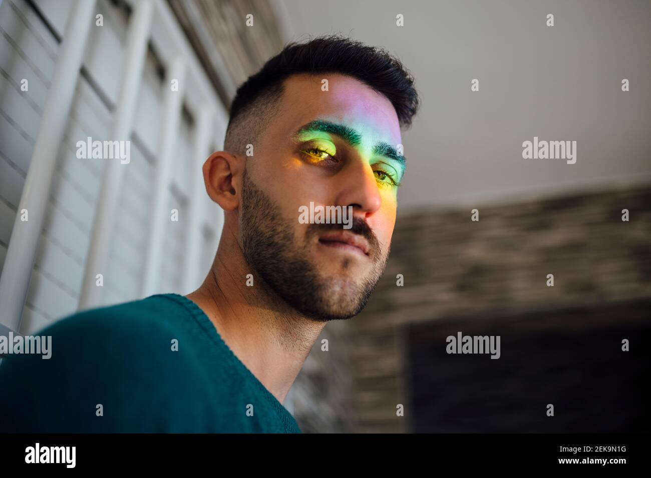 Luce arcobaleno che colpisce il volto del giovane uomo che guarda verso il basso fotocamera Foto Stock