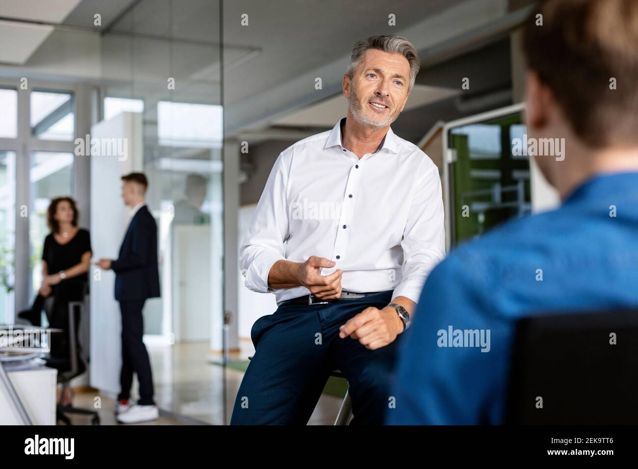 Uomini d'affari che hanno discusso mentre si siedono con un collega in background in un ufficio open plan Foto Stock