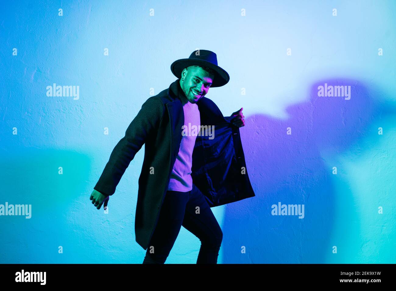 Uomo sorridente che tiene la giacca mentre balla su sfondo colorato Foto Stock