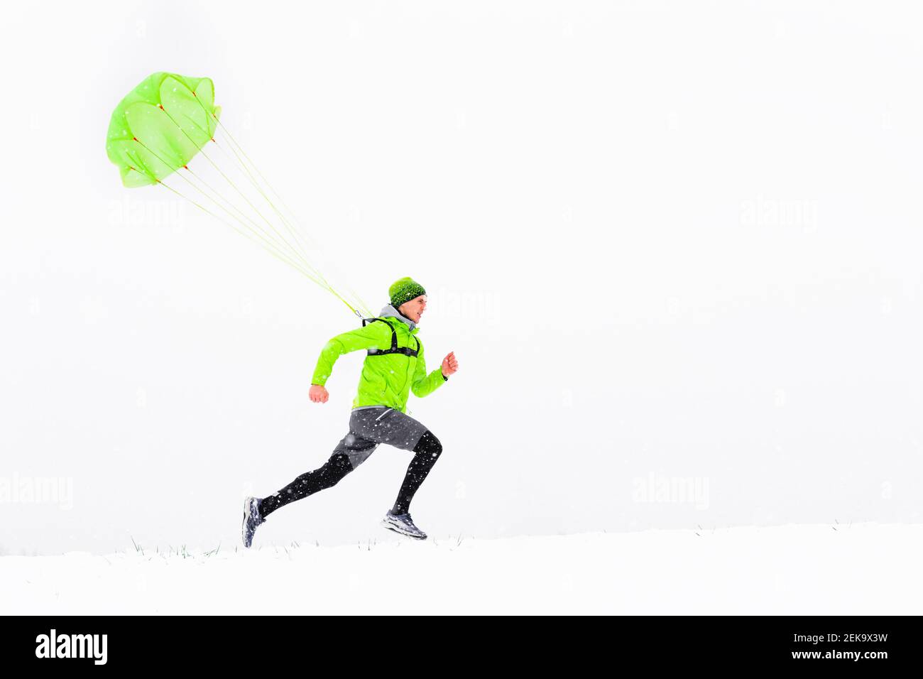 Atleta maschile con paracadute che corre sulla neve durante l'inverno Foto Stock