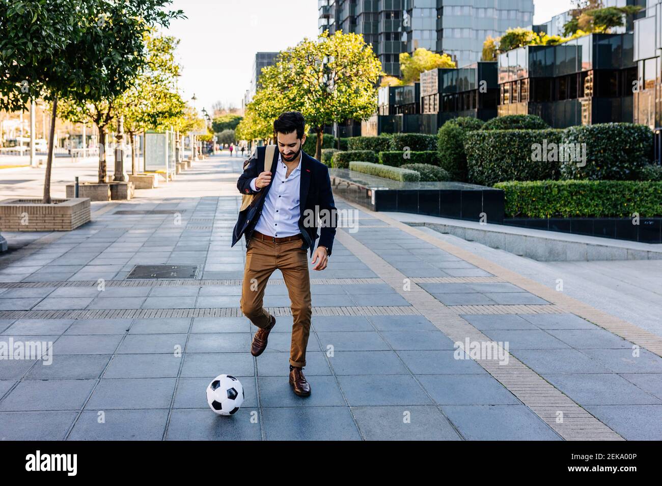 Uomo d'affari che gioca con la palla di calcio mentre corre sul sentiero Foto Stock